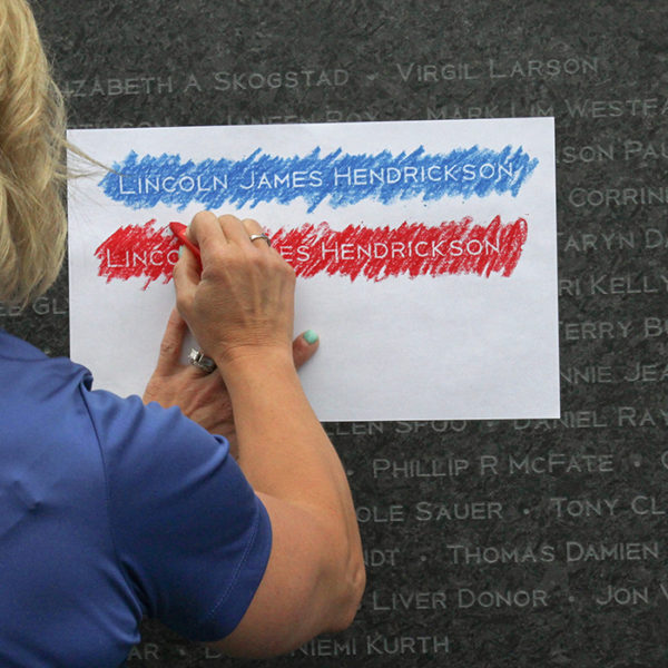 A woman making a crayon rubbing of a name from the LifeSource donor memorial wall